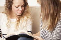 Teen friends sitting on the sofa and reading the Bible together.