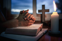 Bible with candlelight and praying hands