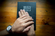 Hands pray on the holy Bible placed on a wooden table on Sunday. worship prayer and bible study concept.