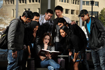 A diverse group of young people look at a book together.
