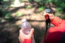 Close up hand hiker man holding bottle of water and hiking poles in forest