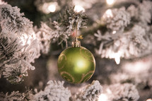 green ball ornament on a flocked Christmas tree 
