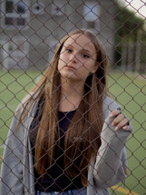 teen girl looking through a chain link fence 