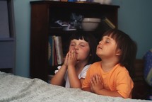 praying children kneeling beside a bed