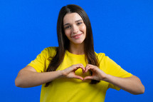 Kind pretty woman making sign of shape heart near her chest. Blue background. Women health, volunteering, donation help and love concept. High quality photo