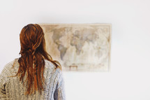 a woman looking at a world map on a wall 