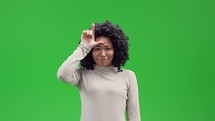 Woman on green screen holding her fingers in the shape of an L on her forehead