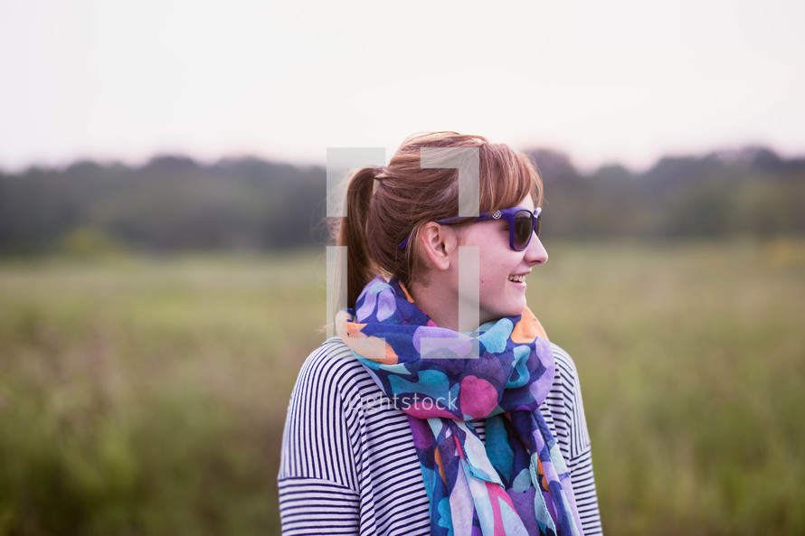 a woman in a scarf and sunglasses standing in a field 