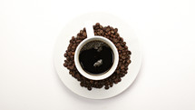 A coffee cup surrounded by coffee beans - isolated on white