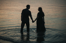 a couple holding hands standing in a pond 