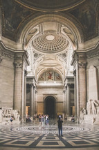 tourists standing in the Pantheon in Paris looking up at the ceiling 