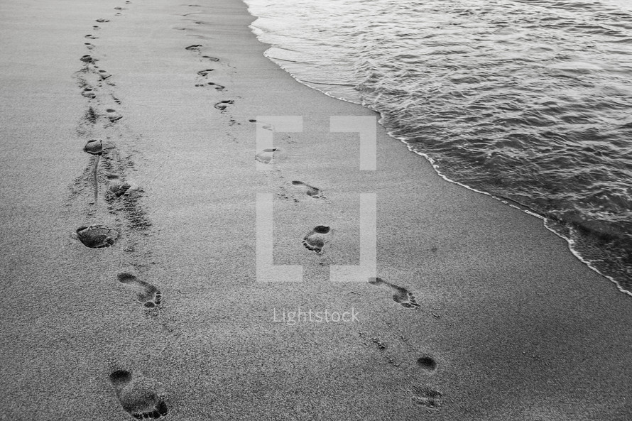 Footprints in the sand on the beach at the shoreline.