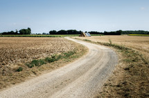 a rural dirt road through a field with hay bales
