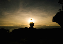 a man standing on a rock overlooking the ocean at sunset