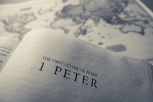 A bible opened to the title page of the first letter of peter (1 peter) with an antique style world map in the background.