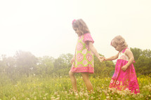 Sisters holding hands walking through field.