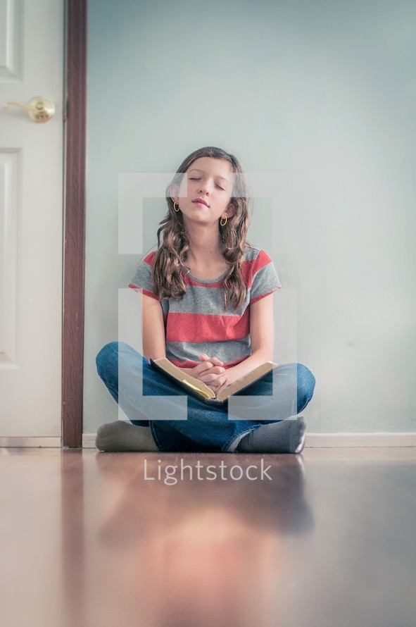 Girl sitting on the floor praying with open bible in her lap