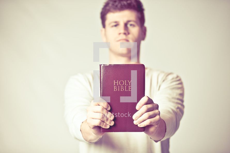 man holding up a red covered Holy Bible