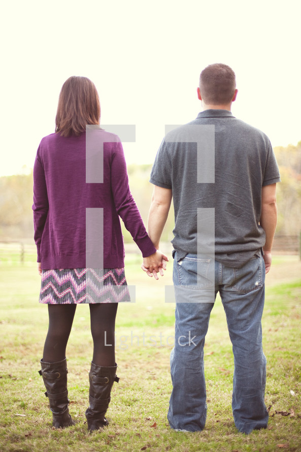 Couple standing in a pasture holding hands.