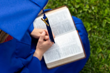 graduate praying over a Bible 