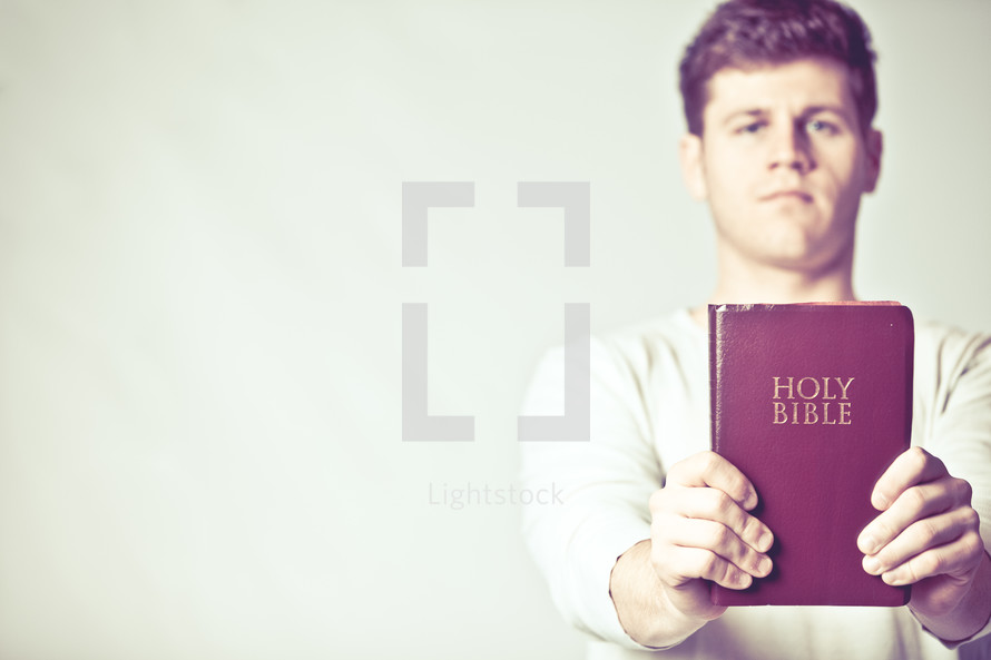 man holding up a red covered Holy Bible