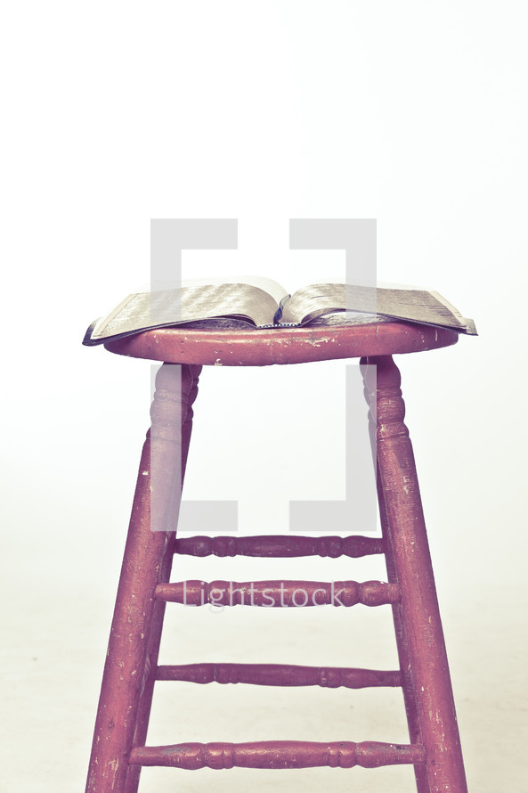 Open Bible op top of wooden stool.