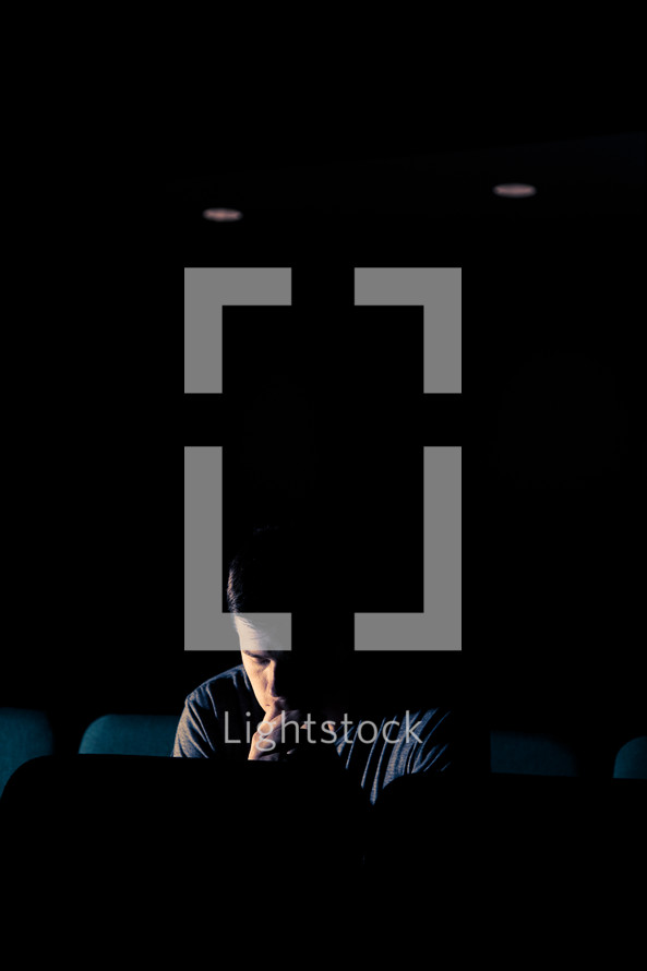 man sitting in an empty auditorium with his head bowed in prayer