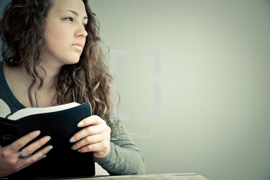 Teenage girl in thought holding open Bible.