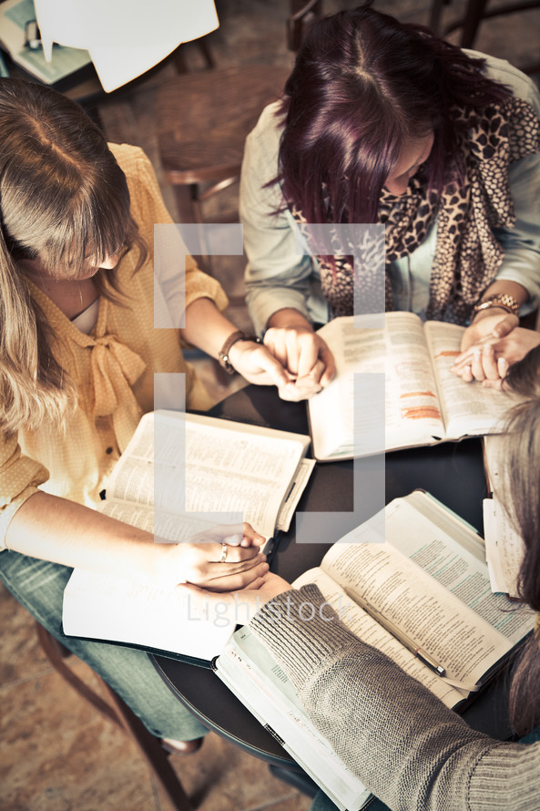 young women holding hands in prayer over Bibles at a Bible study
