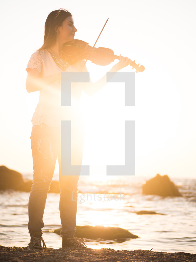Beautiful woman wearing jeans playing the violin on a beach.