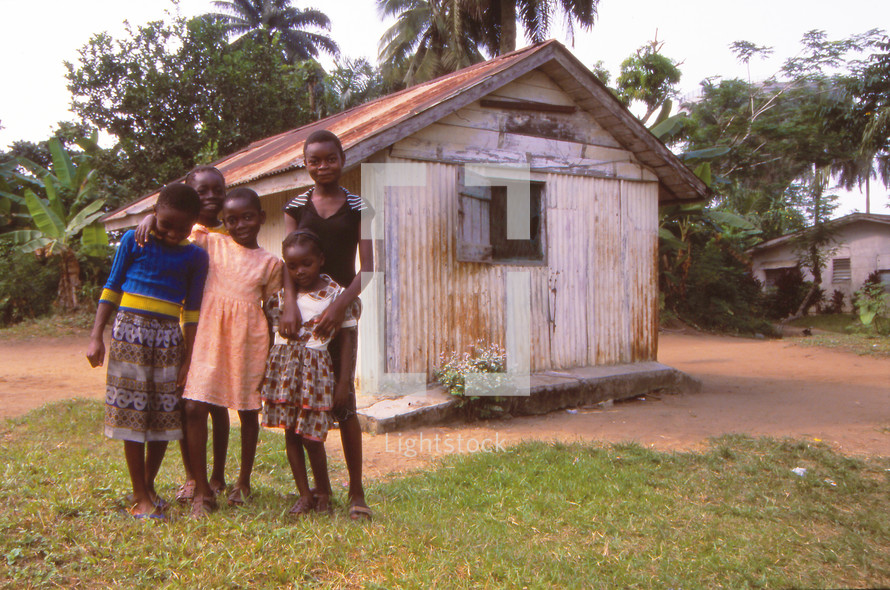 children standing in front of a hut 