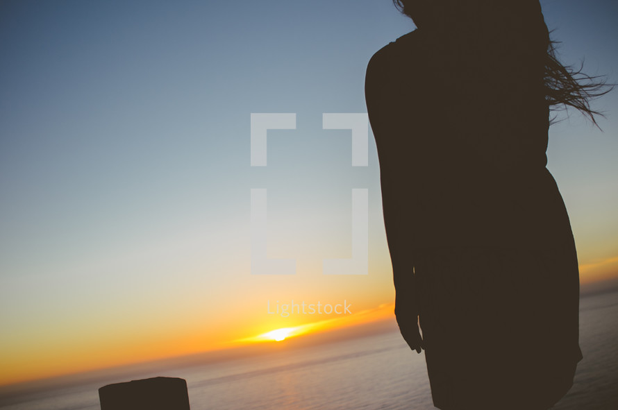 silhouette of a woman at sunset standing near the ocean 