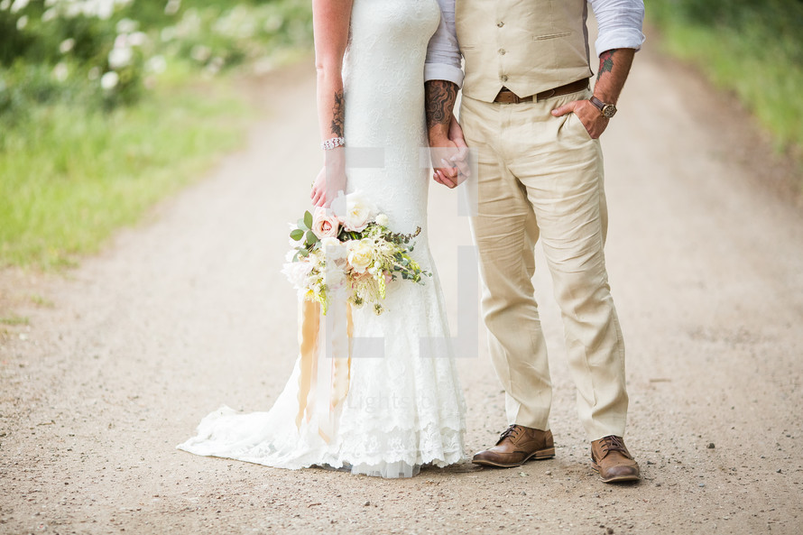 legs of a bride and groom standing on a gravel road 