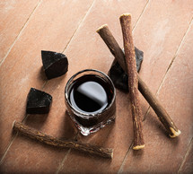 Licorice liqueur with pure blocks and roots on wooden table