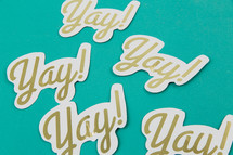 Paper cutouts with the word "yay!" on an aqua background.