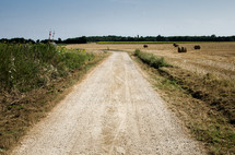 a rural dirt road through a harvested field with hay bales 