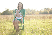 mother sitting in a green chair outdoors holding her infant daughter