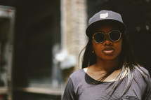 head shot of an African American woman in sunglasses and a ball cap 