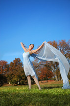 woman dancer, in a green field, autumn trees in the background