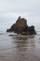 large rock formation jutting out of the ocean water 