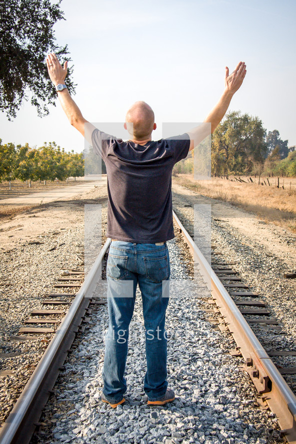 man with arms raised in worship on railroad tracks 