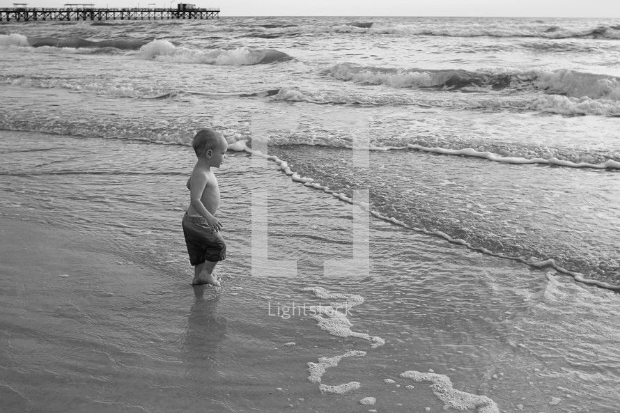 young boy standing in the water at a sandy beach