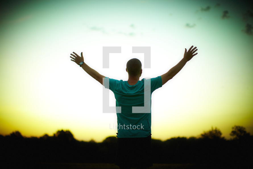 A man, with hands raised, worshipping at sunrise