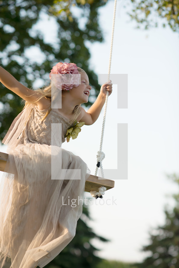 A young girl in a white dress swinging
