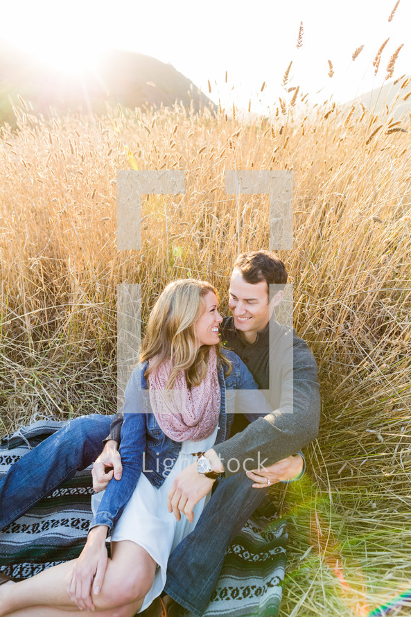 Happy Couple, man woman, sitting on blanket in field of gold tall wheat, embrace, love, romance, smile, engagement, marriage 