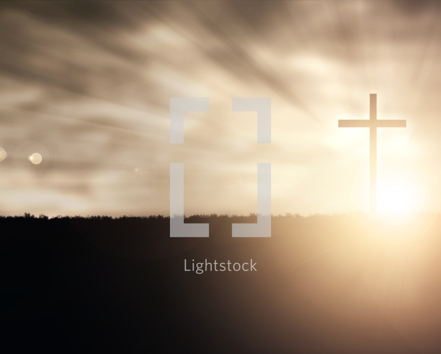 Silhouette of a cross on grassy field at sunset with glowing lights and lens flare.