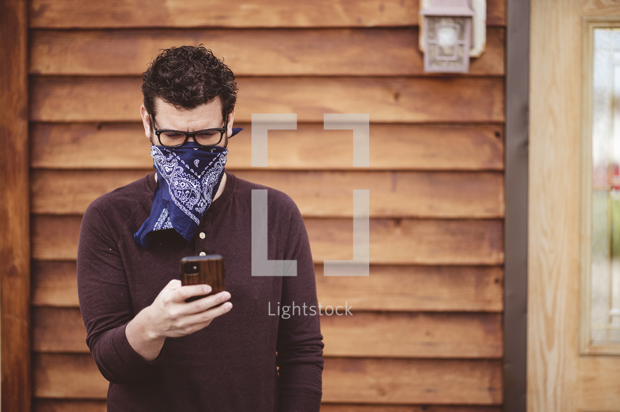 a man with a phone wearing a bandana mask 