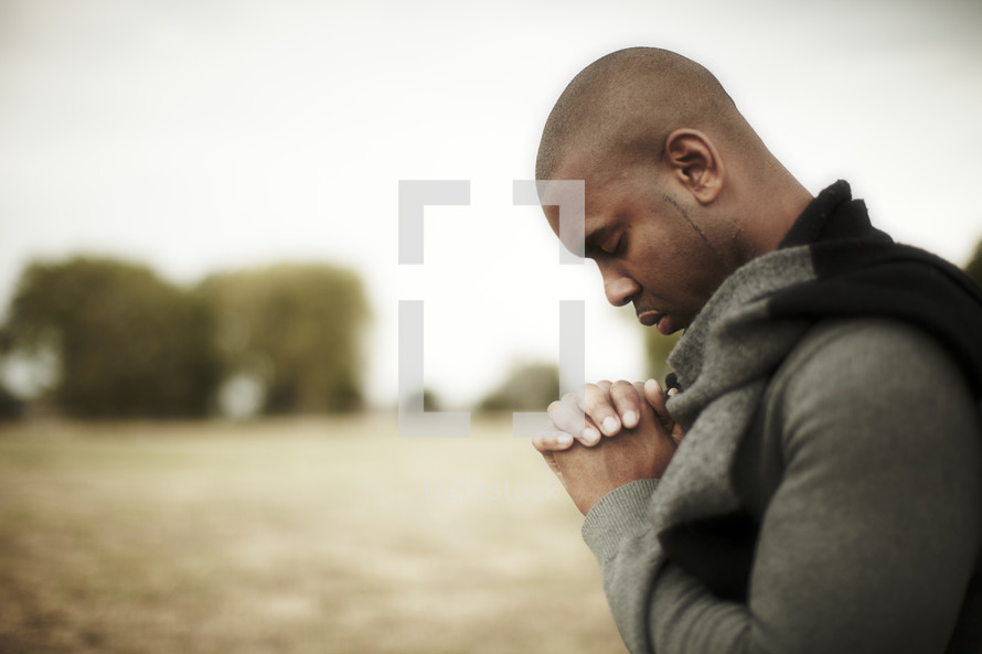 An African American man praying with hands laced