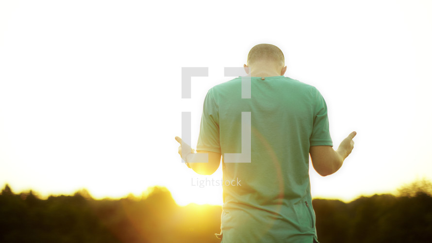 Young adult man worshipping at sunrise.