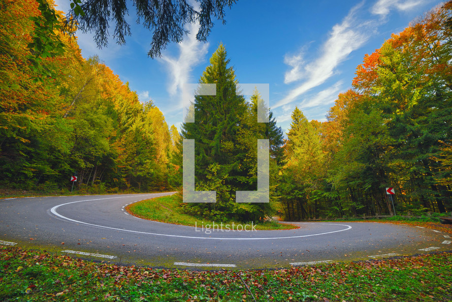 hairpin turn in a mountain road in autumn colored forest at sunrise